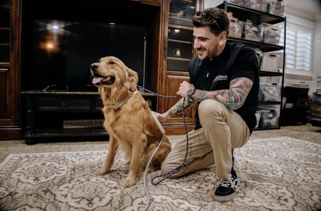 A man kneeling next to his dog while applying PEMF therapy. Picture used by MagnaWavePEMF